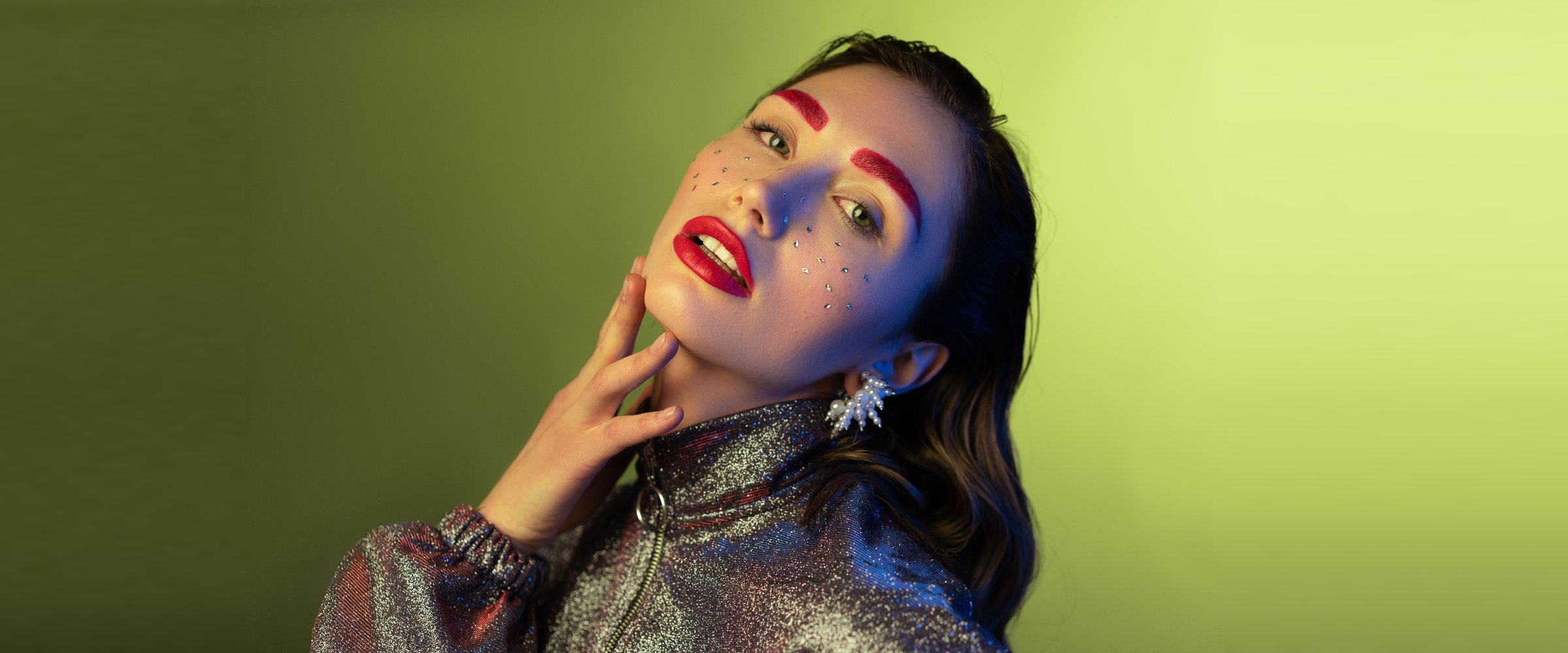 A fashion model in a silver sequined jacket against a lime green backdrop, lit with blue and magenta gels