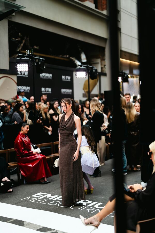 A model in a long dress on a runway with a packed audience on both sides