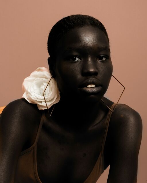 Studio portrait of a woman with a white rose earring against a warm beige backdrop