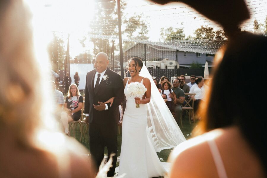 A father walking the bride down an outdoor aisle in the evening sun