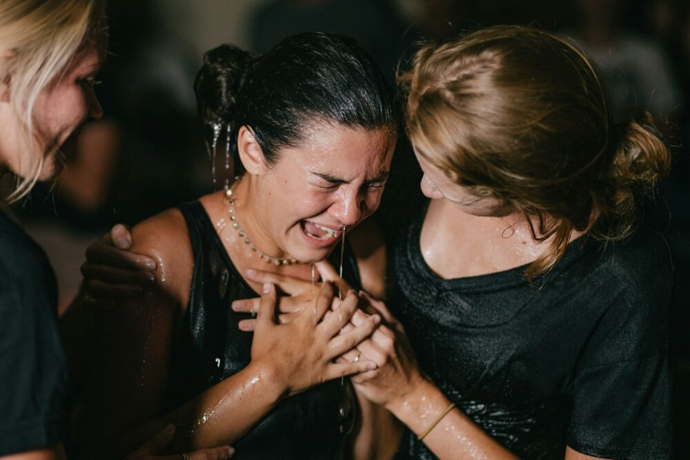 Two women crying and laughing, hands clasped, at a wedding reception