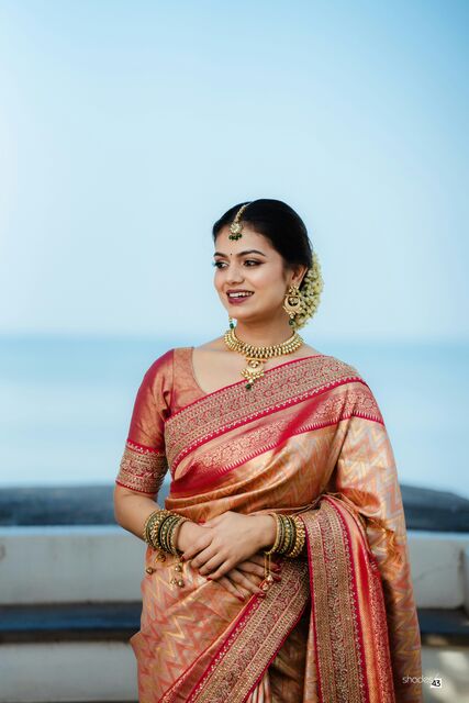 A bride in a red and gold saree smiling against a blue sky